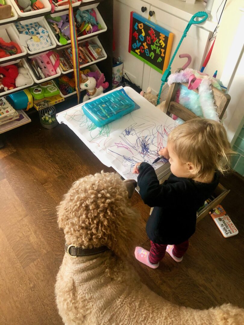 A toddler scribbling on paper next to a dog